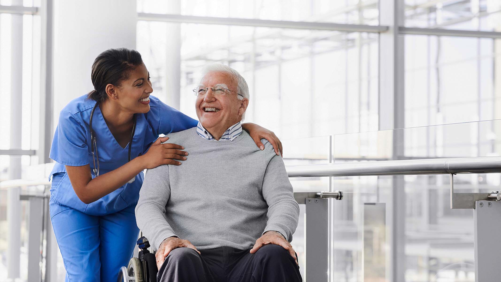 Senior man in a wheelchair, smiling and laughing with a nurse.