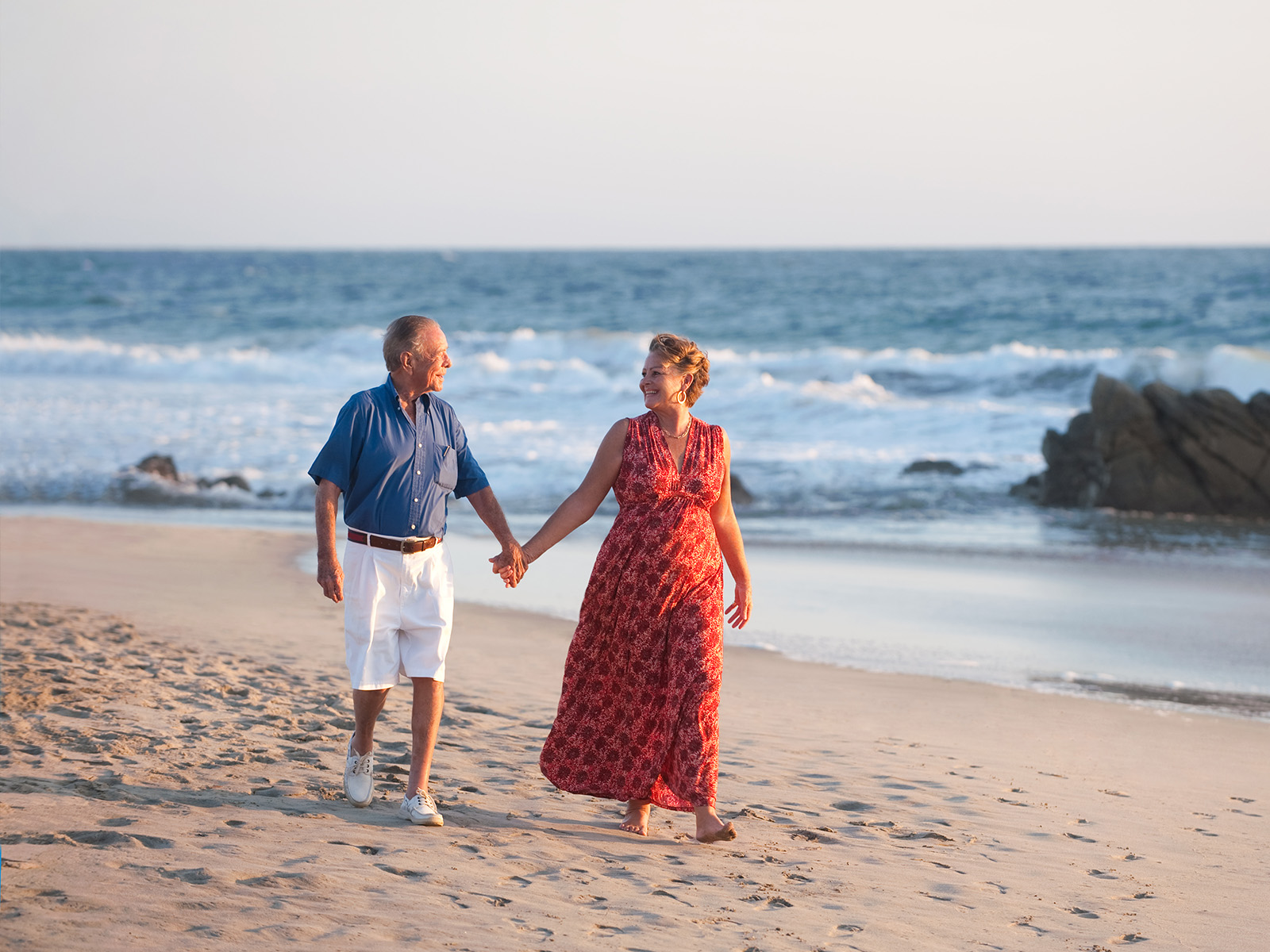 Pareja adulta caminando de la mano en la playa.