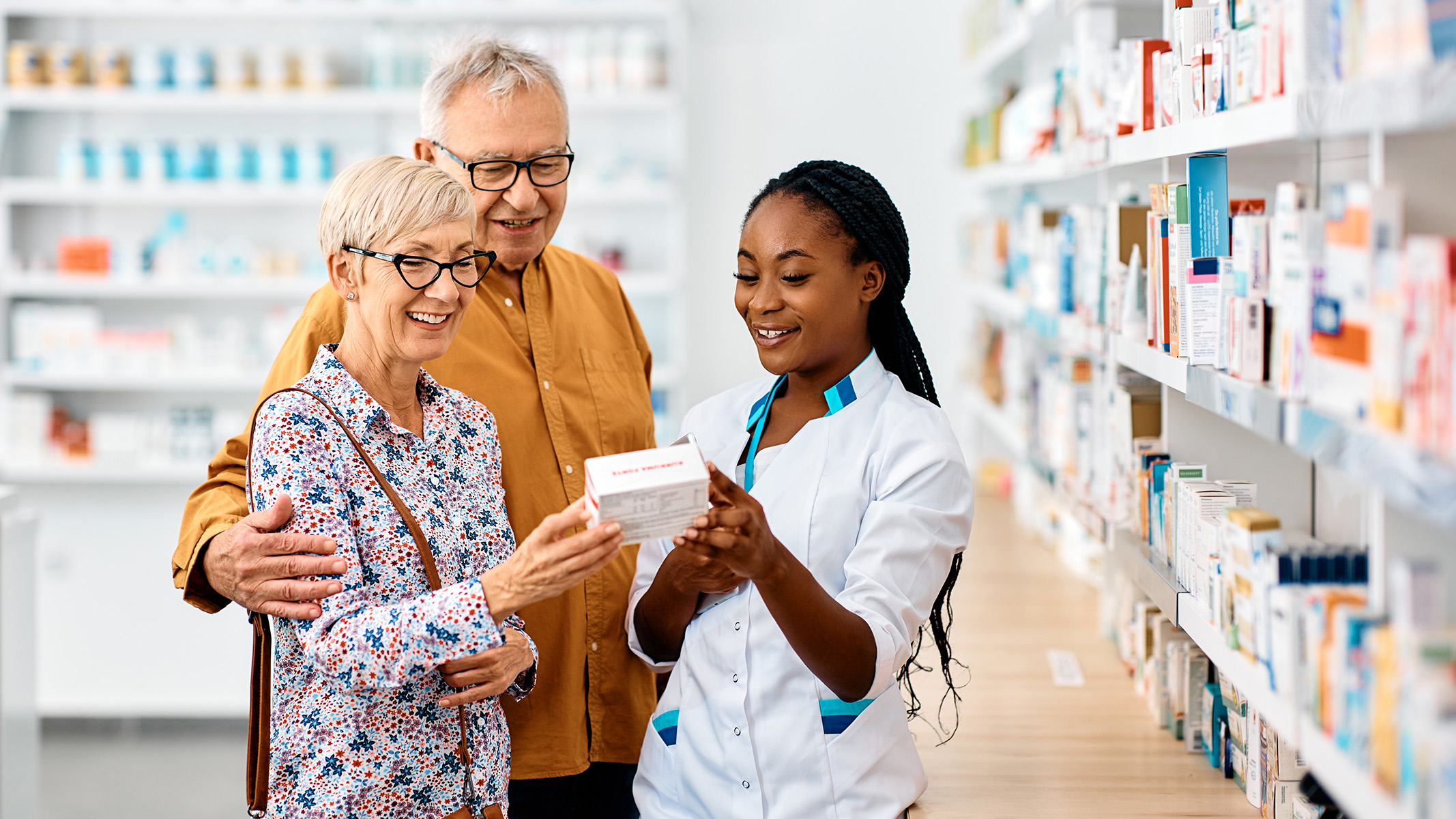 Farmacéutico/a le muestra opciones de medicamentos a una pareja de personas de la tercera edad.