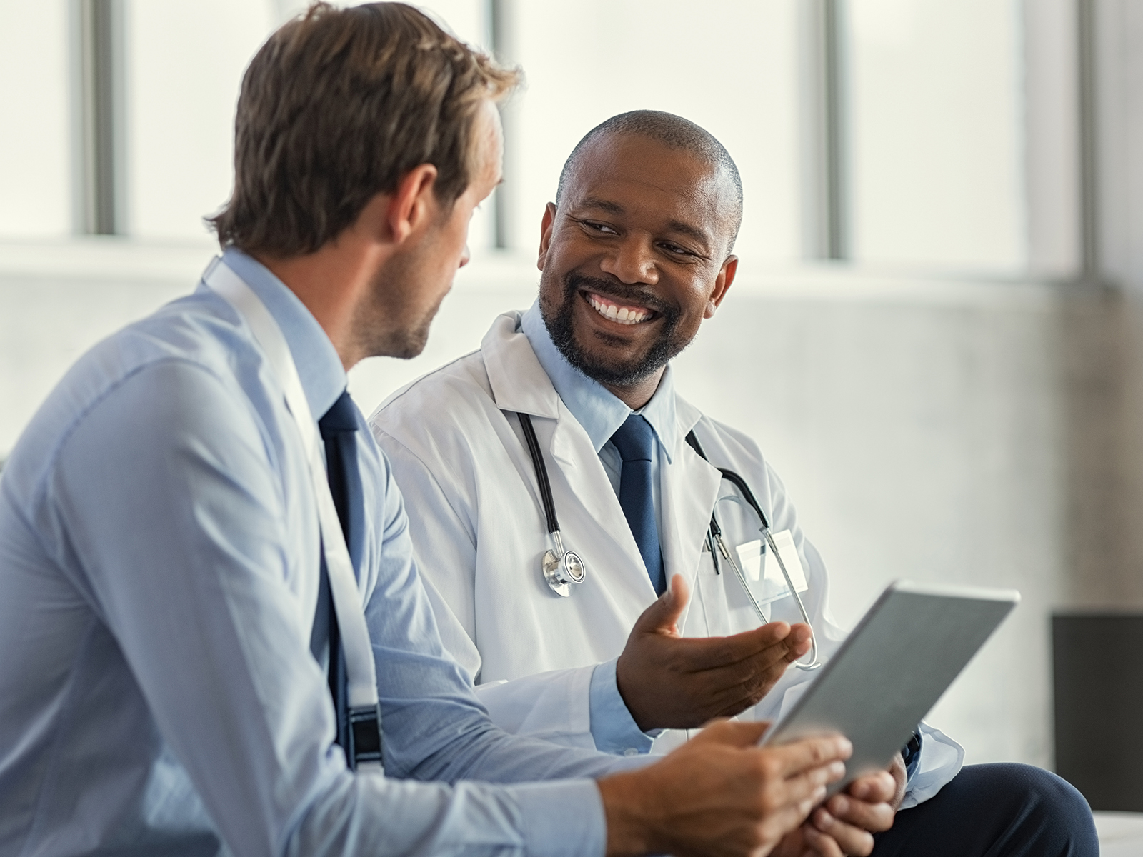 Two male doctors having a conversation while looking at a digital tablet.