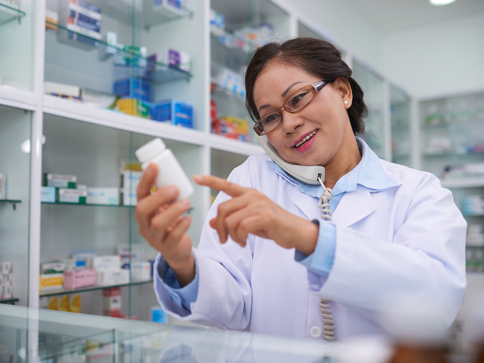 Farmacéutico leyendo la etiqueta de un medicamento mientras habla por teléfono.