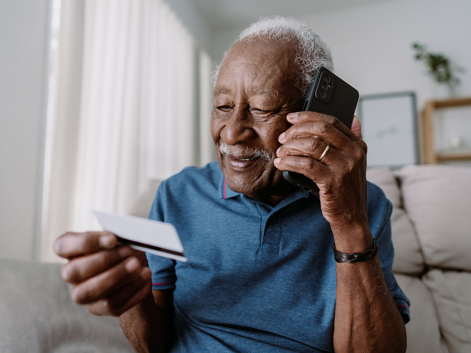Senior man smiling and sitting on couch with card while on the phone