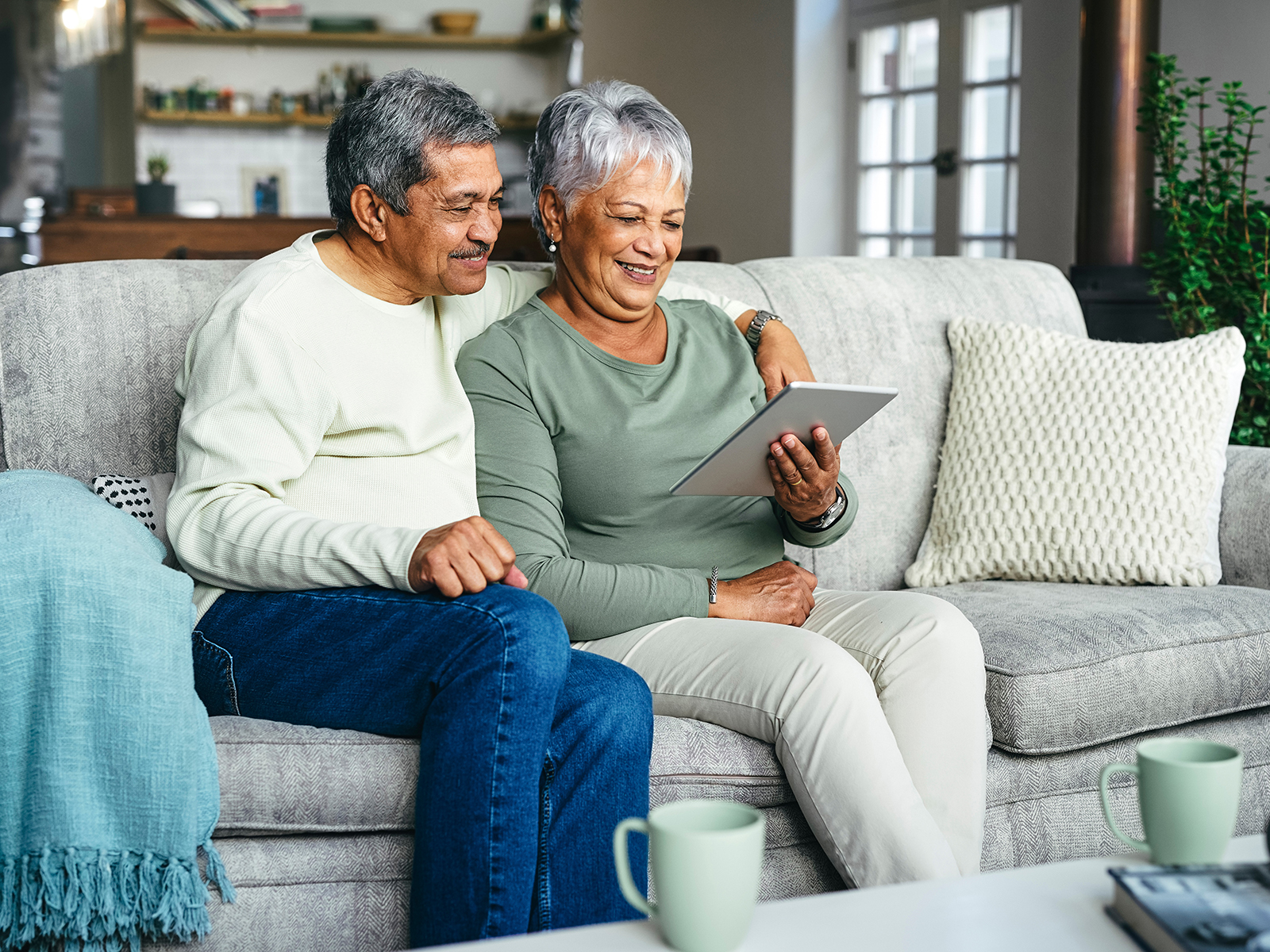 Senior couple sitting on a couch smiling while looking at tablet.