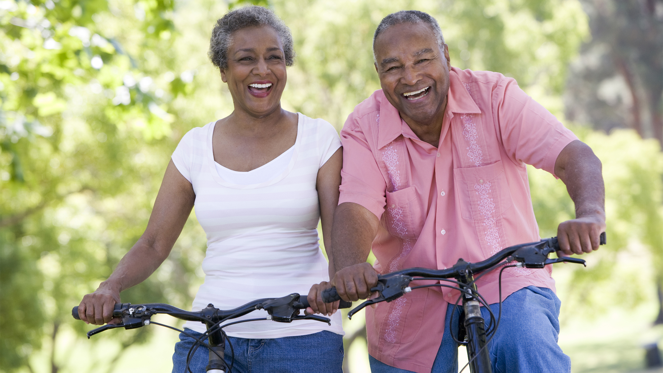 Pareja mayor sonriendo mientras andan en bicicleta.