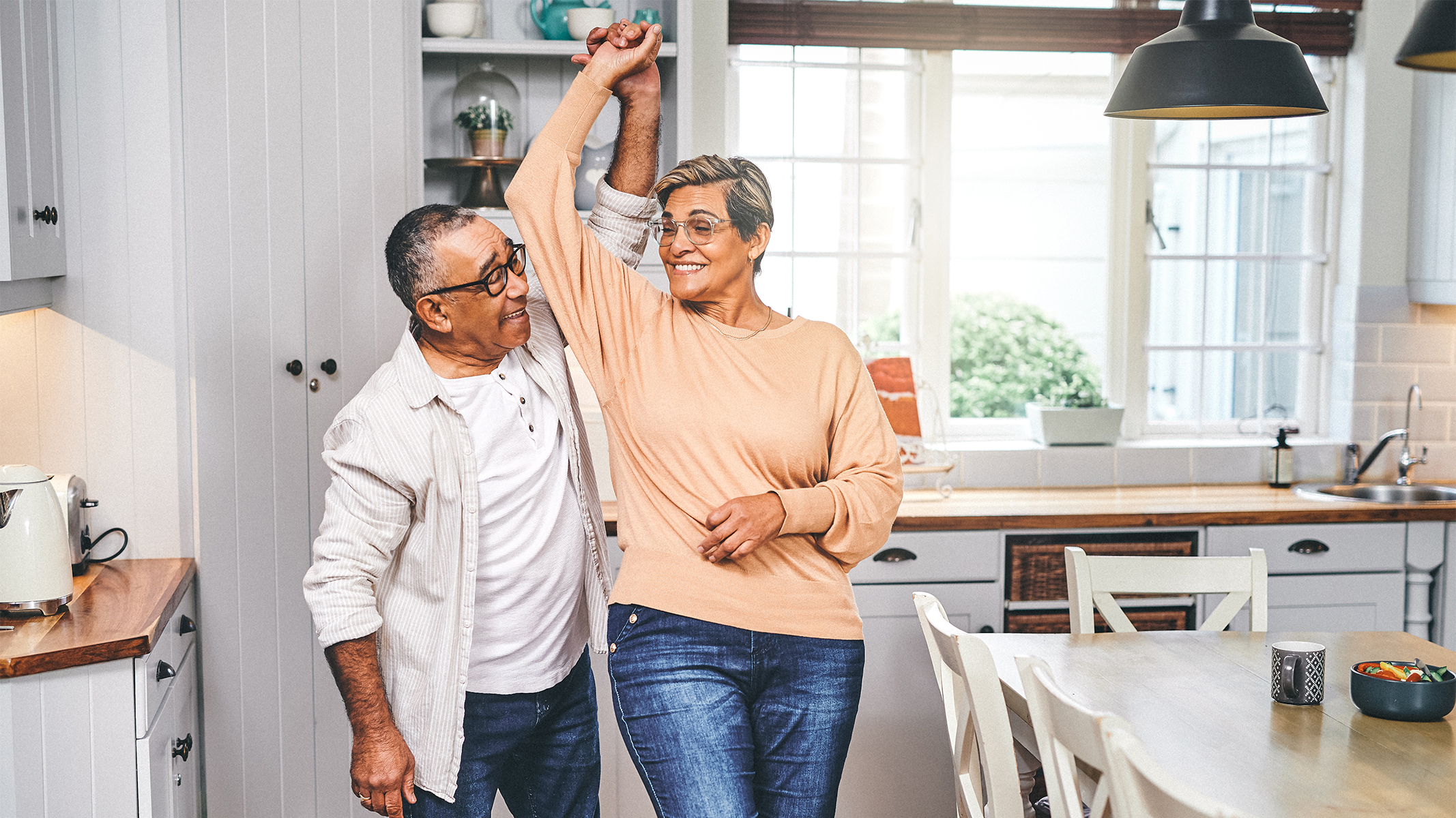 Pareja de personas mayores bailando en la cocina.