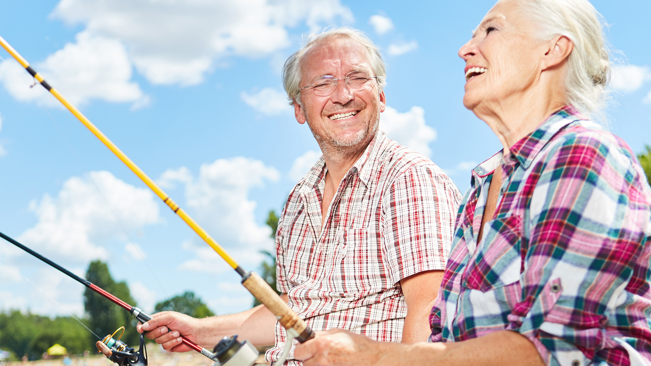 Senior couple sitting on a dock smiling while fishing.