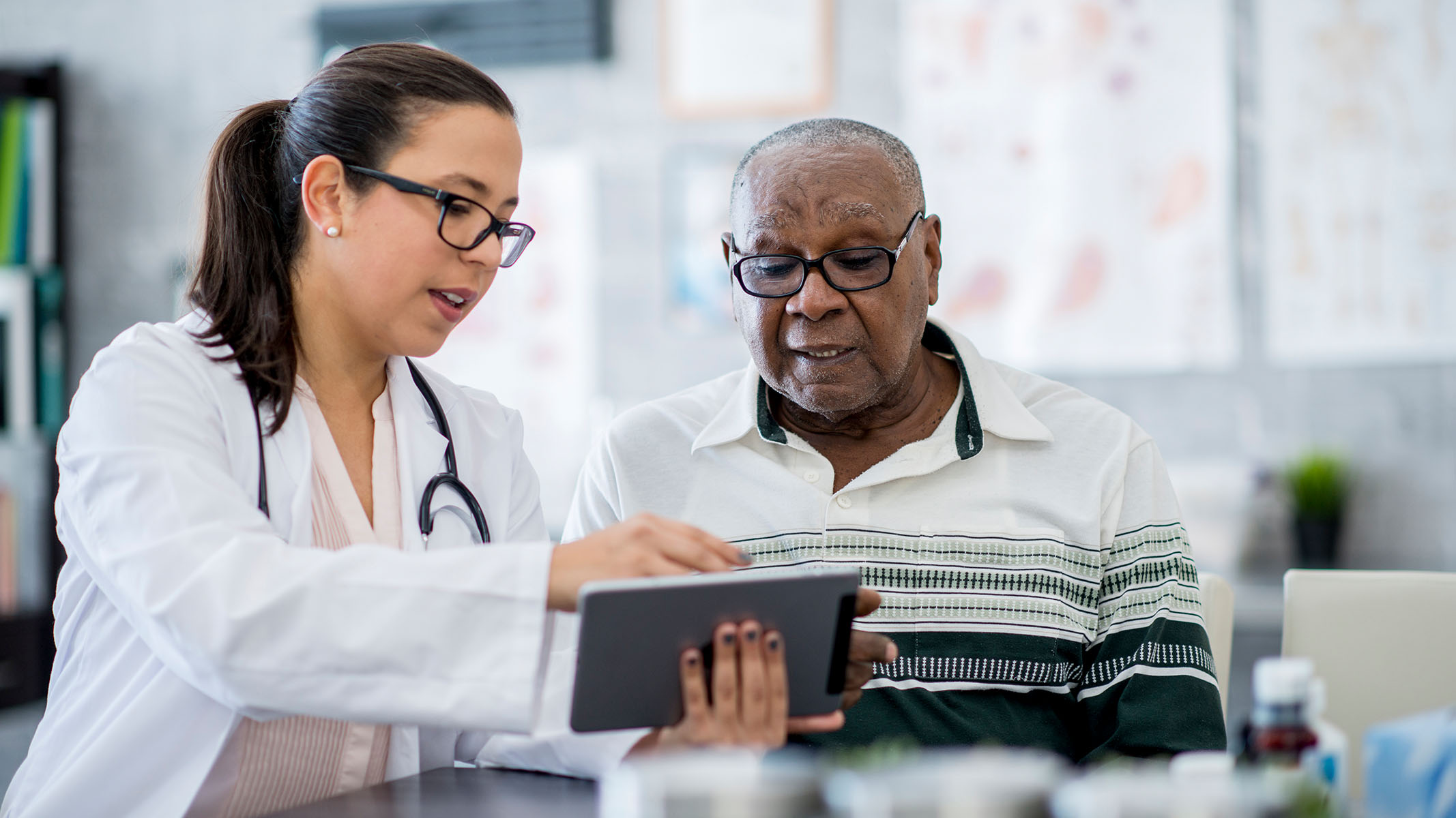 Médico señalando una tablet y hablando con un paciente mayor