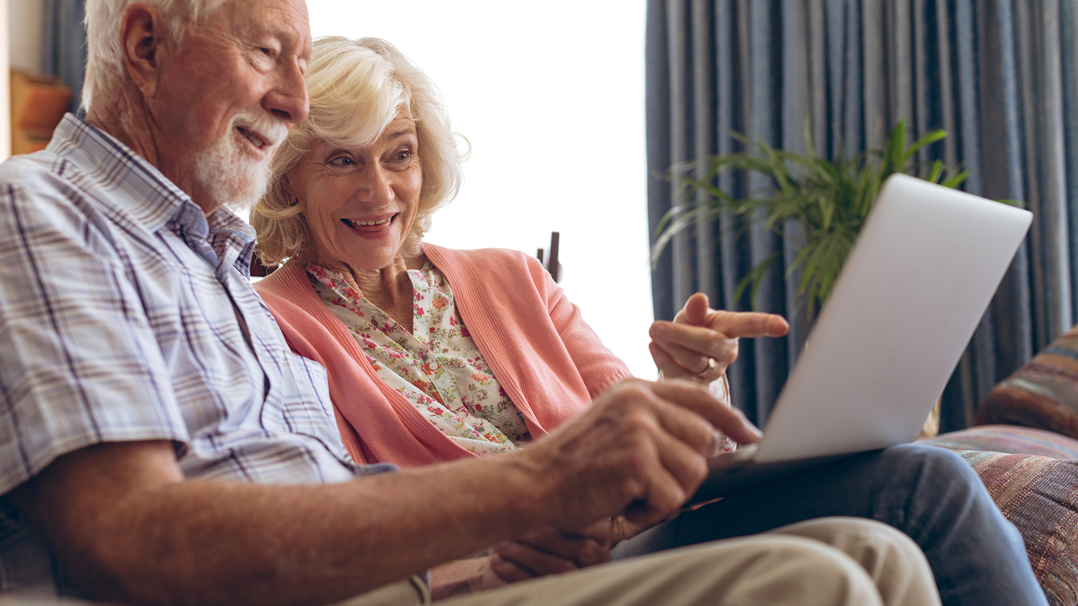 Senior couple on couch pointing at laptop screen.