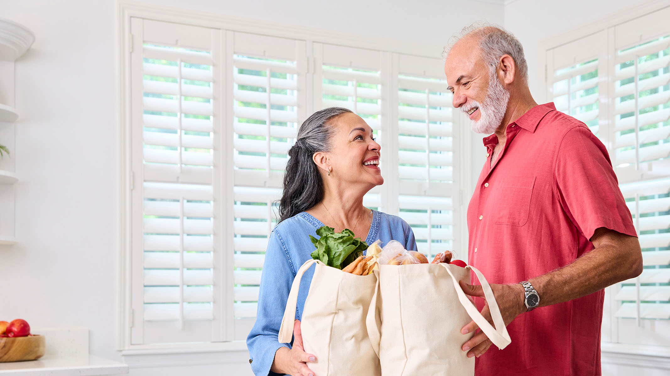 Senior couple with grocery bags in kitchen.
