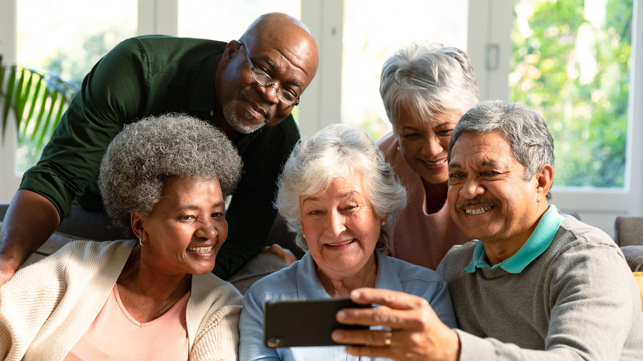 Group of seniors sitting on sofa and looking at smartphone.