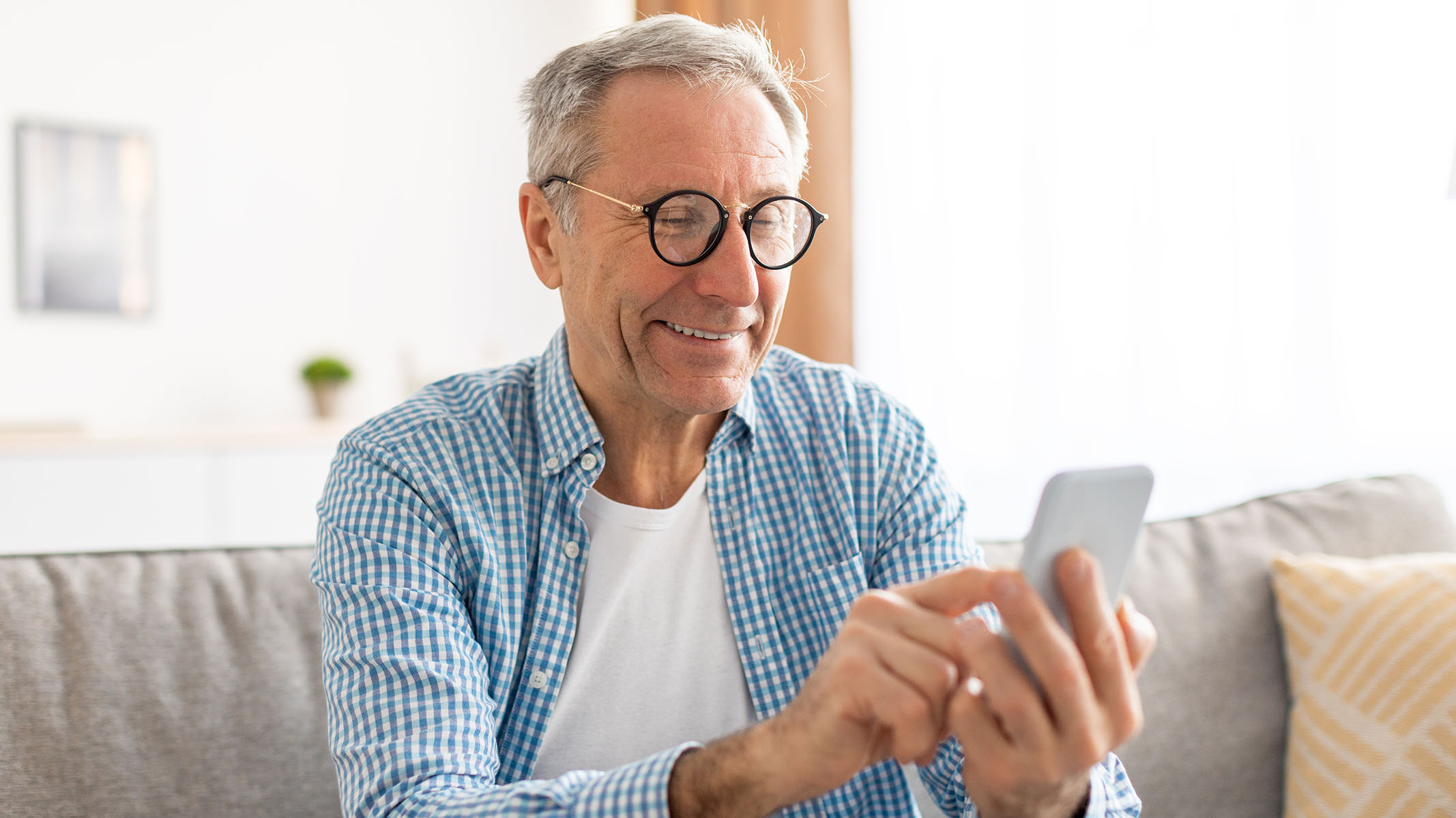 Senior man using smartphone sitting on couch.